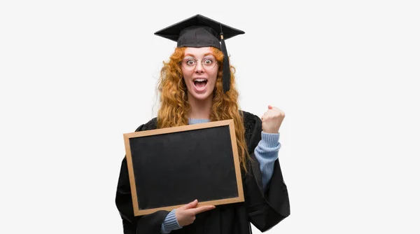 身穿毕业制服的年轻红发学生女子手持黑板尖叫着自豪和庆祝胜利和成功非常兴奋 欢呼的情绪 — 图库照片