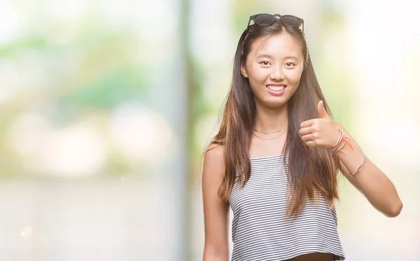 年轻的亚洲妇女戴着太阳镜在孤立的背景下做高兴的拇指手势与手 批准表达式看相机与显示成功 — 图库照片