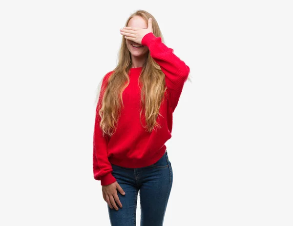 ブロンド十代の若者女性身に着けている赤いセーター笑顔と笑い顔を驚きの目を覆って手します 視覚障害者の概念 — ストック写真