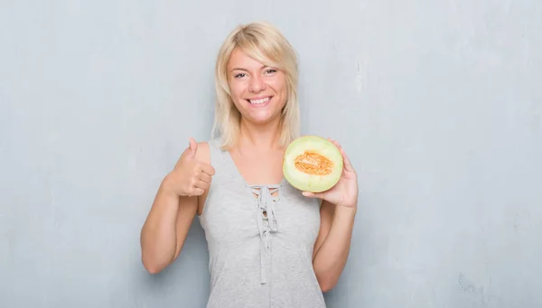 グランジ以上大人の白人女性灰色壁笑顔の サイン 優秀な兆候を親指をやって幸せなメロンを食べる — ストック写真