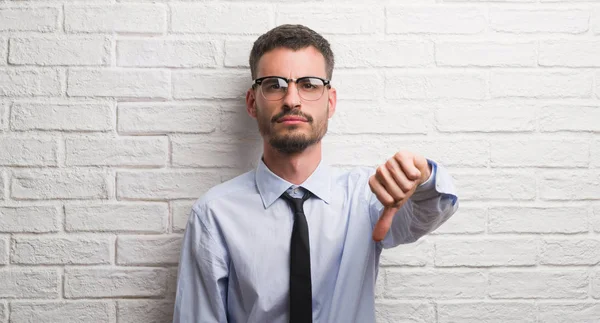 年轻的商界男子站在白色砖墙与愤怒的脸 消极的迹象显示不喜欢拇指向下 拒绝概念 — 图库照片