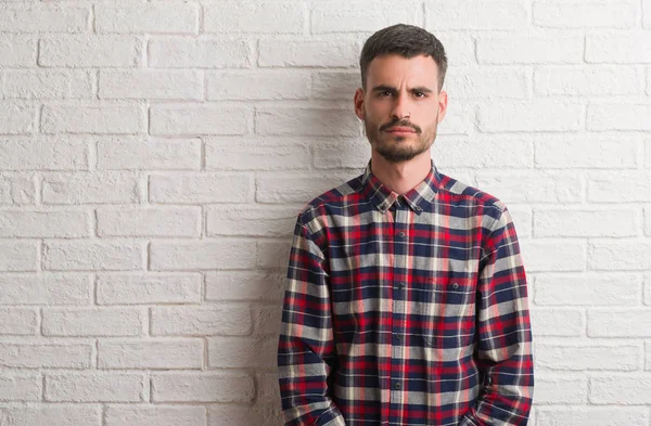 Çatık genç yetişkin adam ayakta beyaz tuğla duvar şüpheci ve gergin, sorunu nedeniyle üzgün. Negatif kişi.