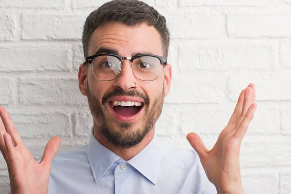 Beyaz tuğla üzerinde duran genç yetişkin iş adamı çok mutlu ve heyecanlı, kazanan ifade büyük gülümseme ile çığlık zaferini kutluyor duvar ve ellerini kaldırdı