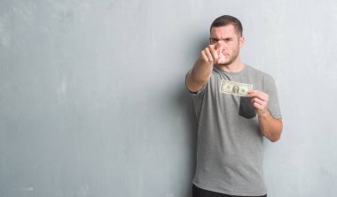 Beyaz delikanlı bir kamera ve size parmak ile işaret dolar gösterilen gri grunge duvarın üzerinden, el işareti, pozitif ve kendinden emin bir jest ön