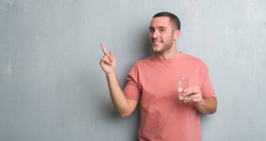 Bir bardak su ile el ve parmak tarafına işaret çok mutlu içme gri grunge duvarın üzerinden beyaz delikanlı