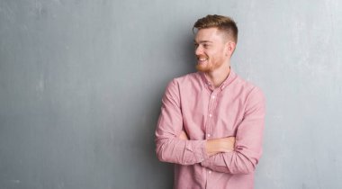 Görünümlü yan ve dik dik bakma uzağa düşünce gülümseyen genç redhead gri grunge duvar giyen üzerinde pembe gömlek uzun kol.