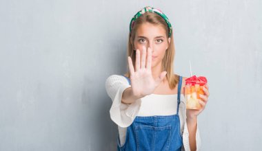 Güzel genç kadın açık eliyle dur işareti ile ciddi ve kendine güvenen ifade, savunma jest yapıyor meyve yeme grunge gri duvarın üzerinden