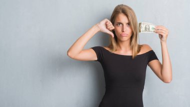 Kızgın yüz, eksi işareti aşağı antipati başparmak ile gösterilen, ret kavramı ile bir dolar tutan grunge gri duvar güzel genç kadın