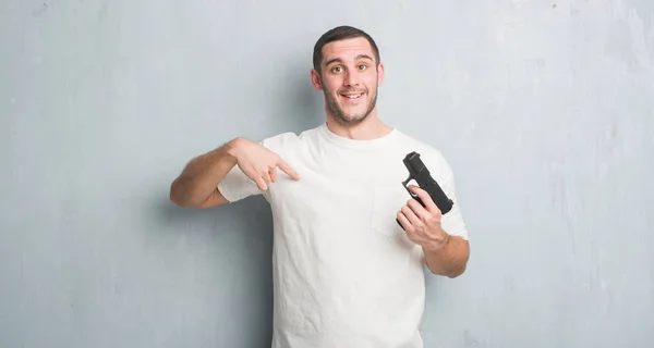 Young Caucasian Criminal Man Grey Grunge Wall Holding Gun Surprise — Stock Photo, Image