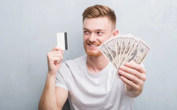 Homem Ruivo Jovem Segurando Dólares Cartão Crédito Sorrindo Olhando Lado — Fotografia de Stock