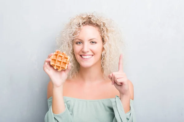 Joven Rubia Sobre Fondo Gris Grunge Comiendo Gofres Belgas Sorprendida — Foto de Stock