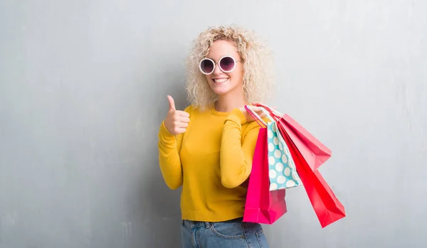 Jovem Mulher Loira Sobre Grunge Fundo Cinza Segurando Sacos Compras — Fotografia de Stock