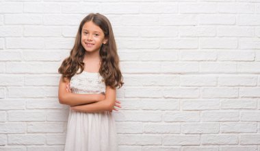 Genç İspanyol çocuk için beyaz tuğla duvar mutlu yüz çapraz silah kameraya bakarak ile gülümseyen. Olumlu bir kişi.