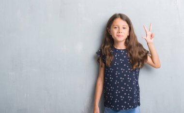 Genç İspanyol çocuğun gösterilen ve parmakları ile işaret grunge gri duvarın üzerinden üçüncü ise kendinden emin ve mutlu gülümseyerek.