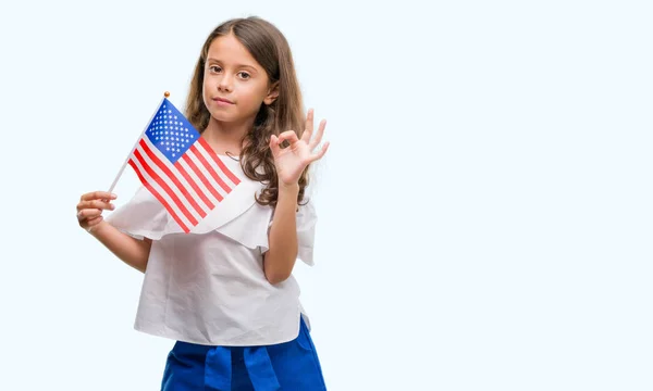 Brunette hispanic girl holding flag of United States of America doing ok sign with fingers, excellent symbol