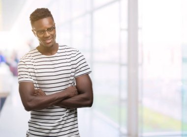 Gözlük ve lacivert t-shirt mutlu yüz ile gülümseyen genç Afro-Amerikan adam kameraya seyir silah geçti. Olumlu bir kişi.