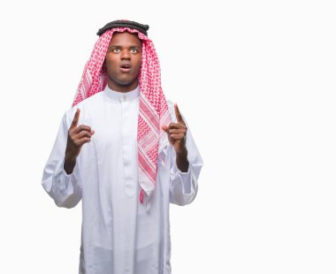 Geleneksel keffiyeh izole arka plan üzerinde giyen genç Arapça Afrika adam hayret ve yukarıya bakıyor ve parmakları ile işaret ve silah kaldırdı şaşırttı.