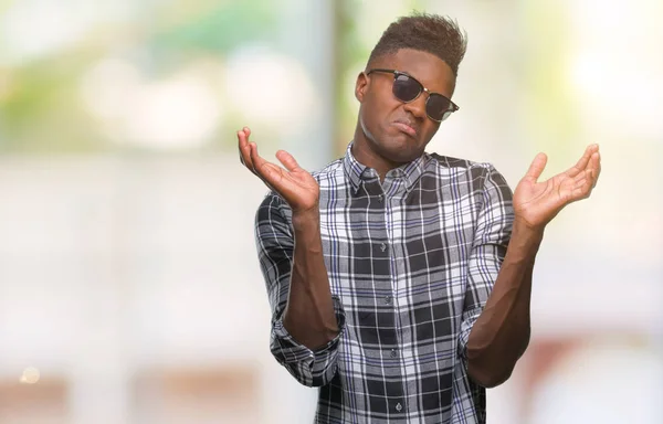 年轻的非洲裔美国人戴着太阳镜在孤立的背景下无能和混淆表达与胳膊和手提出 怀疑概念 — 图库照片