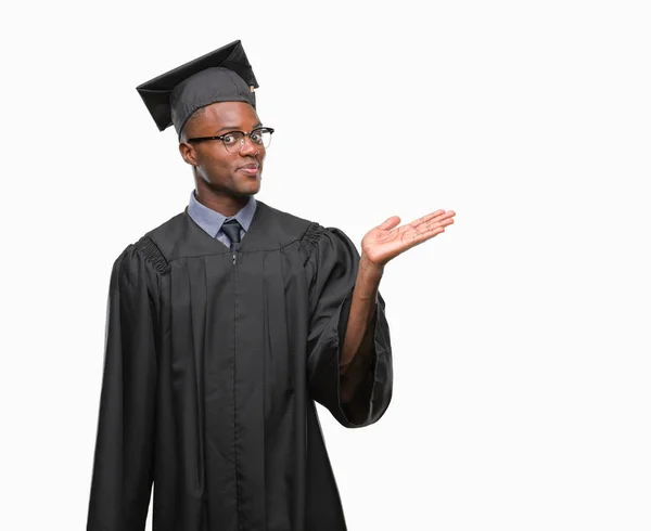 Young graduated african american man over isolated background smiling cheerful presenting and pointing with palm of hand looking at the camera.