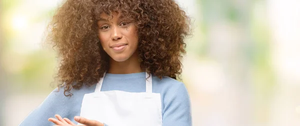 African american shop owner woman wearing an apron holding something in empty hand