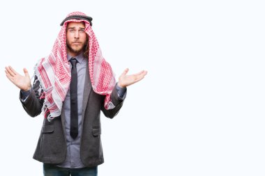 Genç yakışıklı Arap adam uzun saçlı keffiyeh izole arka plan clueless ve şaşkın bir ifadeyle kollar ve eller kaldırdı üzerine giyiyor. Şüphe kavramı.