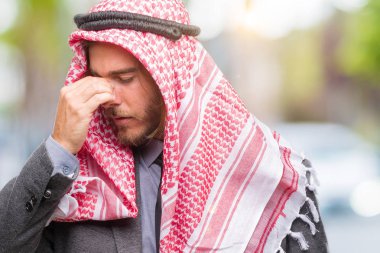Genç yakışıklı Arap adam uzun saçlı keffiyeh izole arka plan yorgun sürtünme burun ve göz yorgunluğu ve baş ağrısı duygu üzerinde giyiyor. Stres ve hayal kırıklığı kavramı.
