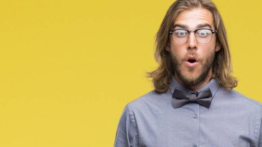 Genç yakışıklı adamla uzun saç giyen papyon korkuyor ve şok sürpriz ifade ile izole arka plan üzerinde korku ve yüz heyecanlı.