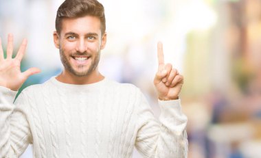 Gösterilen arka plan üzerinde kış kazak giyen genç yakışıklı adam izole ve parmakları ile işaret kendinden emin ve mutlu gülümseyerek süre 6 numara.