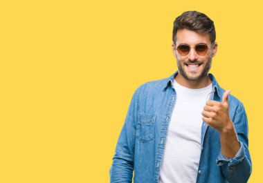 Genç yakışıklı adam hareketi el ile mutlu yaşasın yapıyor izole arka plan üzerinde güneş gözlüğü takıyor. Kameraya bakarak başarı gösteren ile ifade onaylama.
