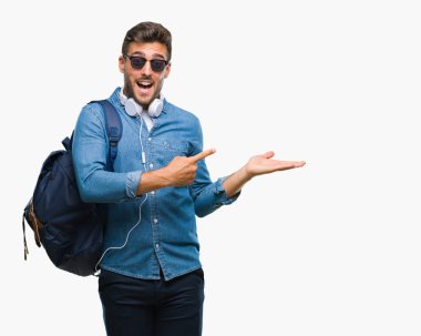 Hayret ve el ile sunulması ve parmak ile işaret ederken kameraya gülümseyen izole arka plan üzerinde kulaklık ve sırt çantası giyen genç yakışıklı turist adam.