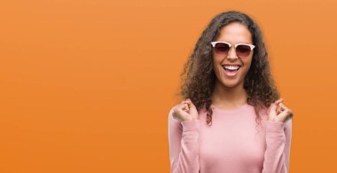 Güzel genç İspanyol kadın kolları olan başarı için heyecanlı güneş gözlüğü takıyor zafer kutluyor gülümseyen kaldırdı. Kazanan kavramı.