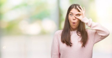 Sürpriz yüz, göz parmaklarının arasından seyir ile ok jest yapıyor bir kazak giyen genç güzel İspanyol kadın şok. İmansız ifade.