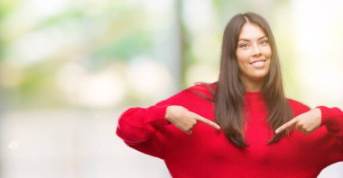 Yüzünde gülümseme ile kendinden emin görünüyorsun, kendini gururlu ve mutlu parmakları ile işaret kırmızı kazak giyen genç güzel İspanyol.