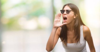 Genç güzel İspanyol bağırarak ve ağzı üzerinde el ile yan için çığlık güneş gözlüğü takıyor. İletişim kavramı.