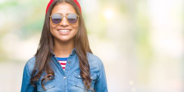 Genç güzel Arap kadın yüzünde mutlu ve güzel bir gülümseme ile izole arka plan üzerinde güneş gözlüğü takıyor. Şanslı kişi.