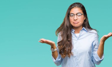 Genç güzel Arap kadın üzerinde gözlük takan arka plan clueless ve şaşkın bir ifadeyle kollar ve eller kaldırdı izole. Şüphe kavramı.