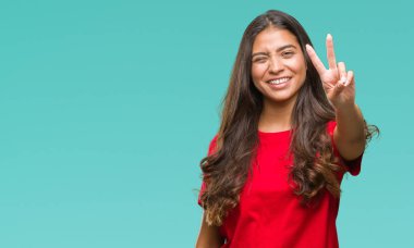 Genç güzel Arap kadın mutlu yüz zafer işareti yaparken kameraya göz kırpıyor ile gülümseyen izole arka plan yüzünden. İki numaralı.