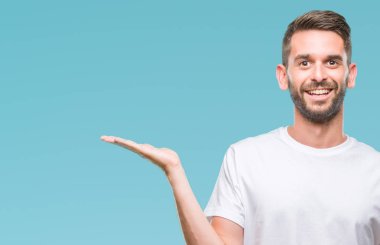 Genç yakışıklı adam neşeli sunulması ve kameraya bakarak avucunun ile işaret gülümseyen izole arka plan üzerinde.