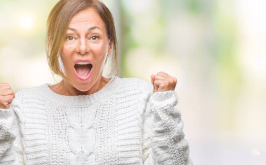 İzole arka plan üzerinde kutluyor kış kazak giyen orta yaş üst düzey İspanyol kadın şaşırttı ve başarı için kaldırdı kollarını açarak hayret ve gözleri açık. Kazanan kavramı.