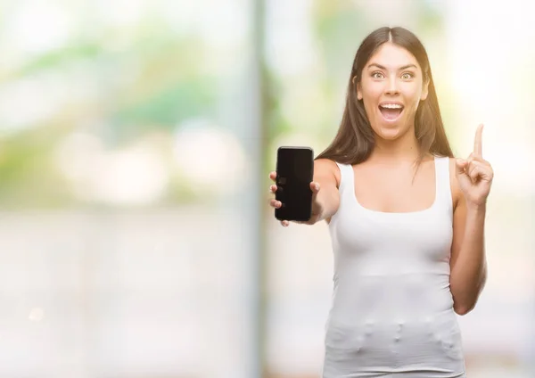 Joven Hispano Hermoso Mostrando Teléfono Inteligente Sorprendido Con Una Idea —  Fotos de Stock