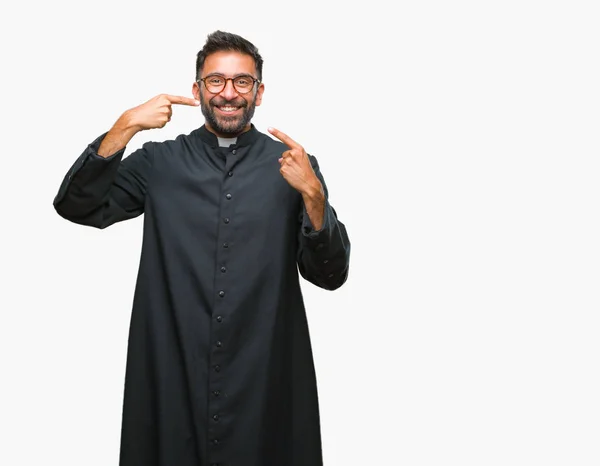 成人拉美裔天主教神父在孤立的背景下微笑着自信地显示和指着手指的牙齿和嘴巴 健康理念 — 图库照片