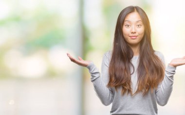 Genç Asyalı kadın yüzünden izole arka plan clueless ve şaşkın bir ifadeyle kollar ve eller kaldırdı. Şüphe kavramı.