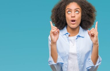 Genç afro Amerikalı kadın üzerinden hayran ve yukarıya bakıyor ve parmakları ile işaret ve silah kaldırdı sürpriz izole arka plan.