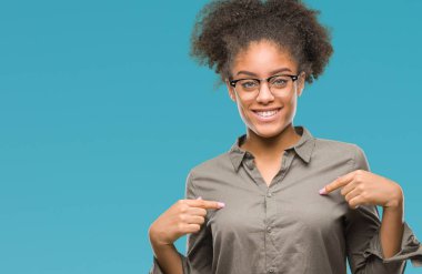Yüzünde gülümseme ile kendinden emin görünüyorsun, kendini gururlu ve mutlu parmakları ile işaret izole arka plan üzerinde gözlük takan genç afro Amerikalı kadın.