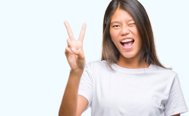 Genç Asyalı kadın mutlu yüz zafer işareti yaparken kameraya göz kırpıyor ile gülümseyen izole arka plan üzerinde. İki numaralı.