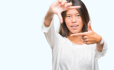 Genç Asyalı kadın elle yapma çerçeve ve parmakları ile mutlu yüz gülümseyen izole arka plan üzerinde. Yaratıcılık ve Fotoğrafçılık kavramı.