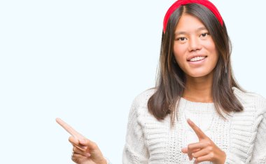 Gülümseyen ve iki elleri ve parmakları ile tarafına işaret kamera bakarak izole arka plan üzerinde kış kazak giyen genç Asyalı kadın.