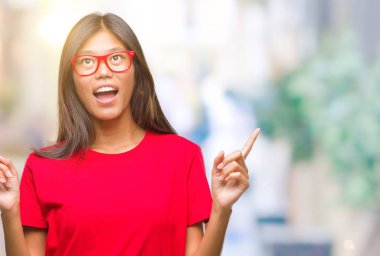 Hayret ve yukarıya bakıyor ve parmakları ile işaret ve silah kaldırdı sürpriz izole arka plan üzerinde gözlüklü Genç Asyalı kadın.