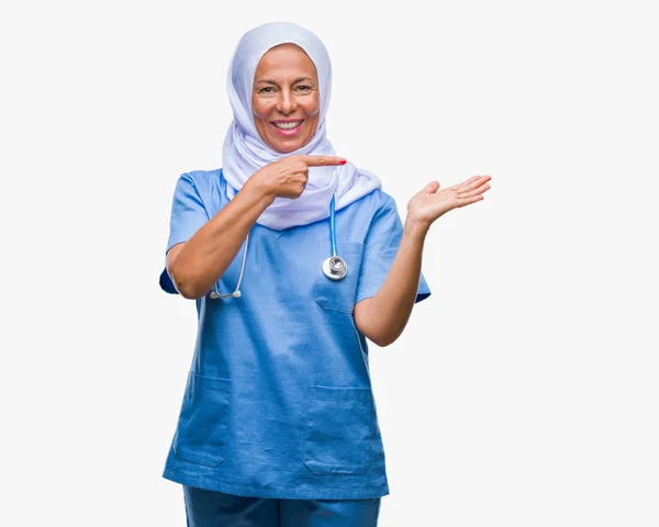 驚くし 手とを提示 指で指している間カメラに笑顔孤立の背景にヒジャーブを着て中年アラブに上級看護師女性 — ストック写真