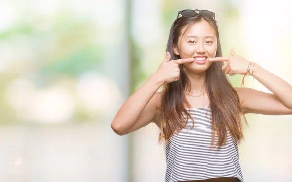 年轻的亚洲妇女戴着太阳镜在孤立的背景下微笑着自信地显示和指着手指的牙齿和嘴巴 健康理念 — 图库照片